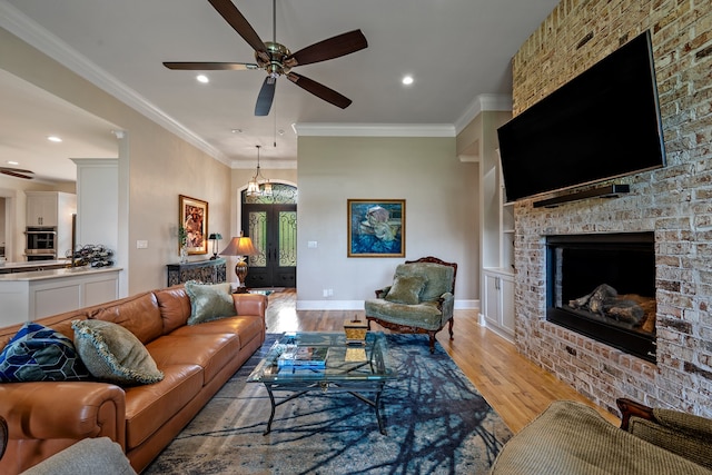 living room with a brick fireplace, ceiling fan, french doors, light hardwood / wood-style flooring, and ornamental molding