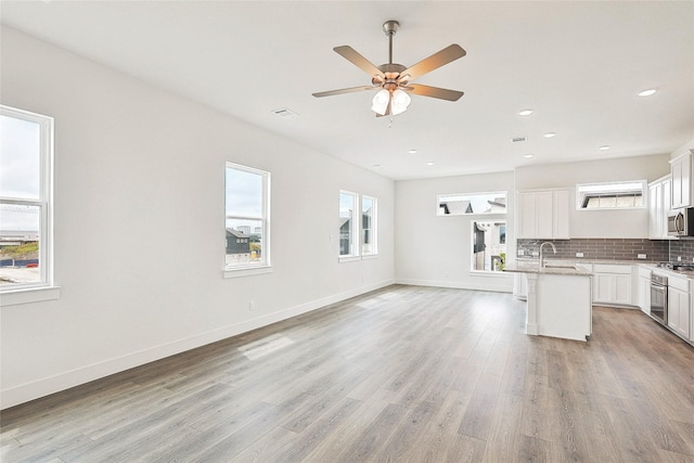 kitchen with appliances with stainless steel finishes, white cabinetry, backsplash, a kitchen island with sink, and light wood-type flooring