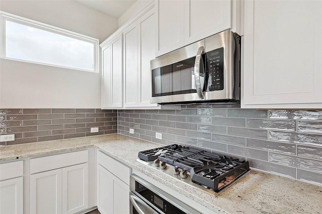 kitchen with stainless steel appliances, white cabinetry, light stone countertops, and decorative backsplash