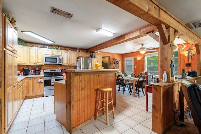 kitchen with appliances with stainless steel finishes, ceiling fan, light tile flooring, and a kitchen bar