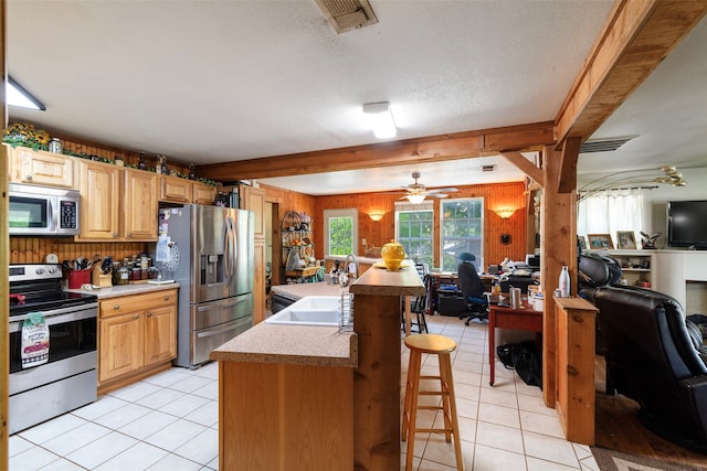 kitchen featuring ceiling fan, light tile floors, sink, a breakfast bar area, and stainless steel appliances