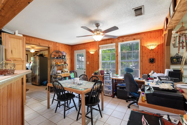 dining area featuring wood walls, ceiling fan, light tile floors, and a textured ceiling