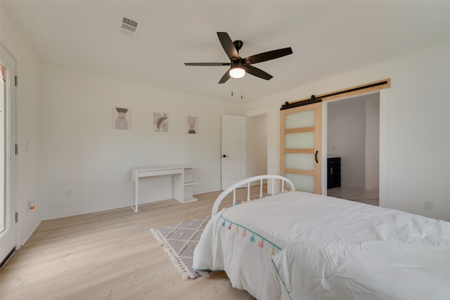 bedroom with light hardwood / wood-style flooring, ceiling fan, and a barn door