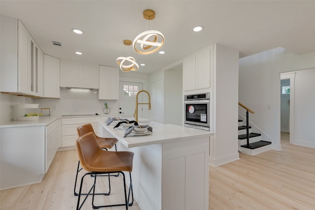 kitchen featuring an island with sink, white cabinetry, and stainless steel oven