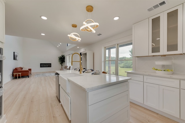 kitchen with hanging light fixtures, light stone counters, white cabinets, a fireplace, and light hardwood / wood-style flooring