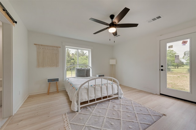 bedroom featuring ceiling fan, light wood-type flooring, a barn door, and access to exterior