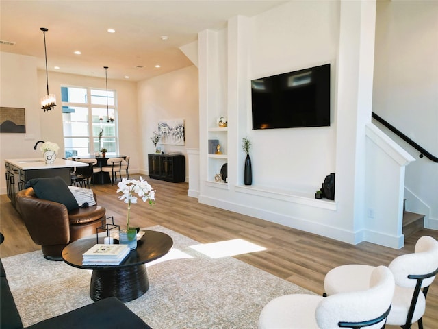 living room with an inviting chandelier, built in features, light hardwood / wood-style flooring, and sink