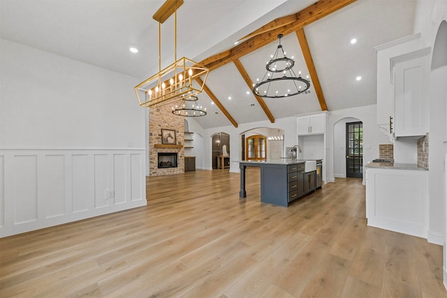 kitchen with hanging light fixtures, a stone fireplace, a kitchen bar, a kitchen island with sink, and white cabinets