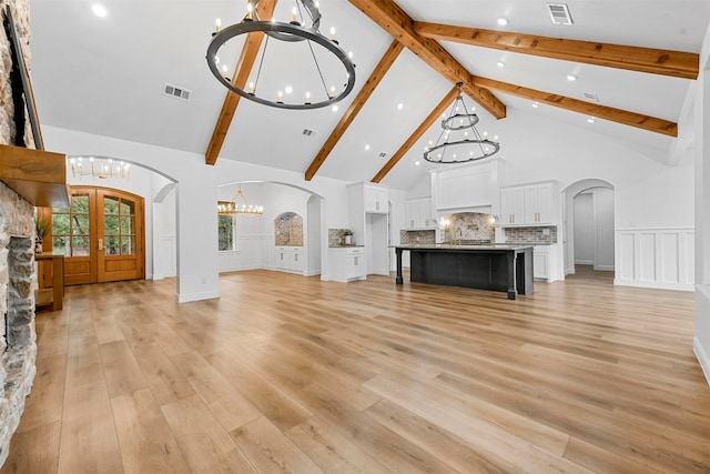 unfurnished living room featuring french doors, beam ceiling, high vaulted ceiling, light hardwood / wood-style flooring, and a notable chandelier