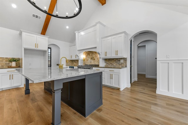 kitchen with backsplash, a kitchen island with sink, sink, beam ceiling, and white cabinets