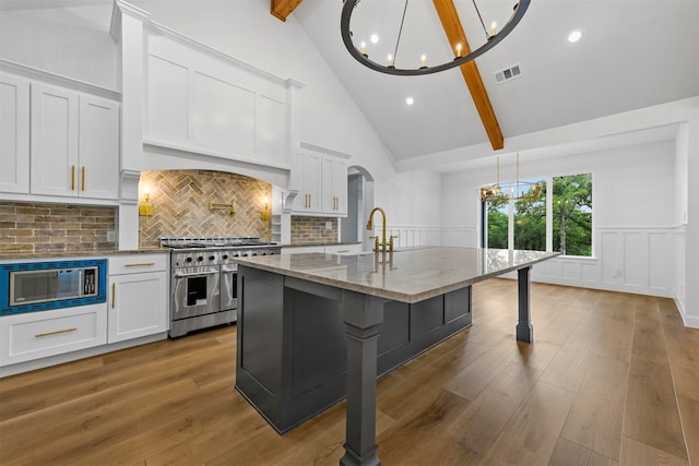 kitchen with beam ceiling, white cabinetry, a center island with sink, and appliances with stainless steel finishes