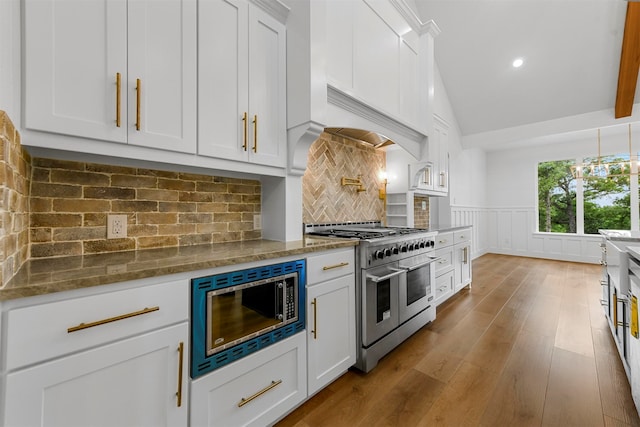 kitchen featuring double oven range, dark stone counters, white cabinets, built in microwave, and tasteful backsplash