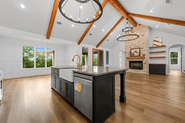 kitchen featuring light stone countertops, dishwasher, sink, a chandelier, and a kitchen island with sink