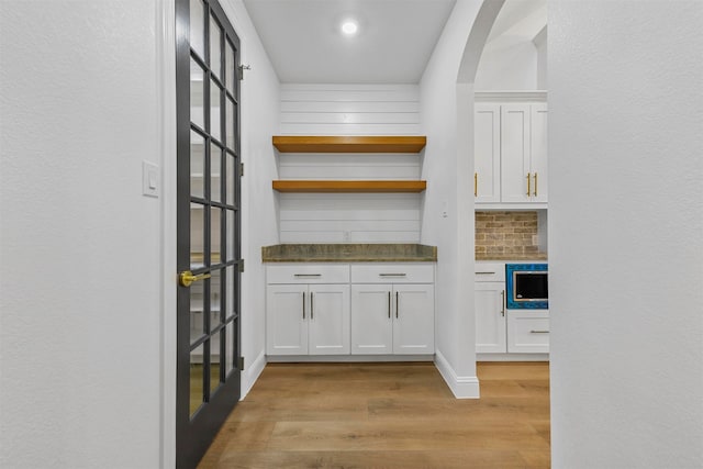 bar with white cabinets, light wood-type flooring, built in microwave, and tasteful backsplash