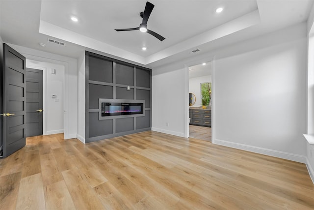 unfurnished living room featuring ceiling fan, a raised ceiling, built in features, and light hardwood / wood-style flooring