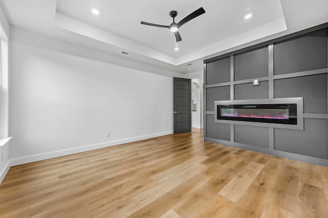 unfurnished living room with ceiling fan, light hardwood / wood-style flooring, and a tray ceiling