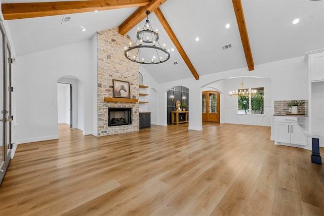 unfurnished living room featuring a notable chandelier, light hardwood / wood-style floors, a stone fireplace, and high vaulted ceiling