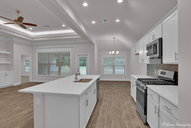 kitchen with stainless steel appliances, light hardwood / wood-style floors, a center island with sink, ceiling fan with notable chandelier, and sink