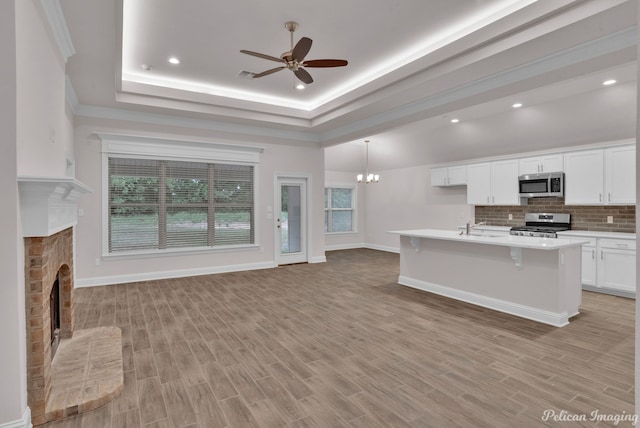 kitchen featuring ceiling fan with notable chandelier, a brick fireplace, stainless steel appliances, a center island with sink, and tasteful backsplash