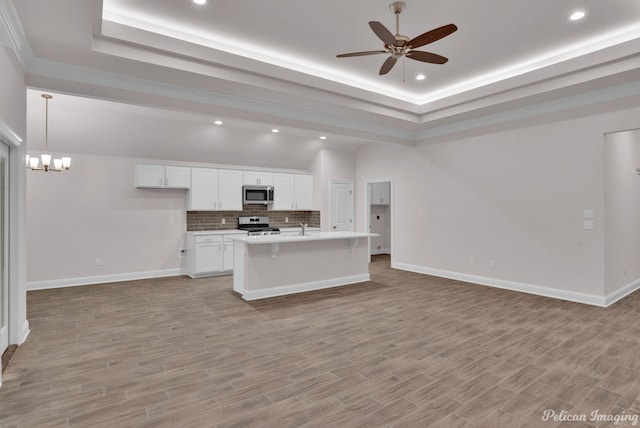 kitchen with white cabinets, ceiling fan with notable chandelier, tasteful backsplash, stainless steel appliances, and a center island with sink