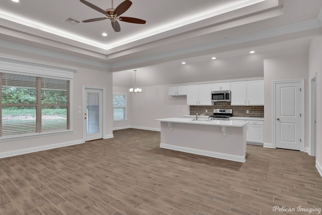 kitchen featuring pendant lighting, a kitchen island with sink, ceiling fan with notable chandelier, backsplash, and appliances with stainless steel finishes