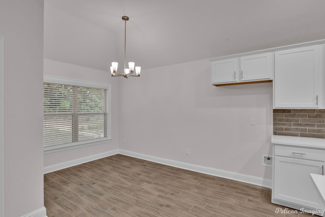 kitchen featuring hanging light fixtures, light hardwood / wood-style flooring, tasteful backsplash, white cabinetry, and an inviting chandelier