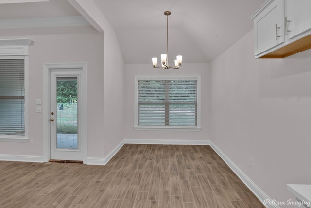 spare room featuring a chandelier, vaulted ceiling, and light wood-type flooring