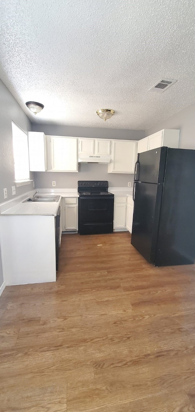 kitchen featuring white cabinets, a textured ceiling, hardwood / wood-style flooring, and black appliances