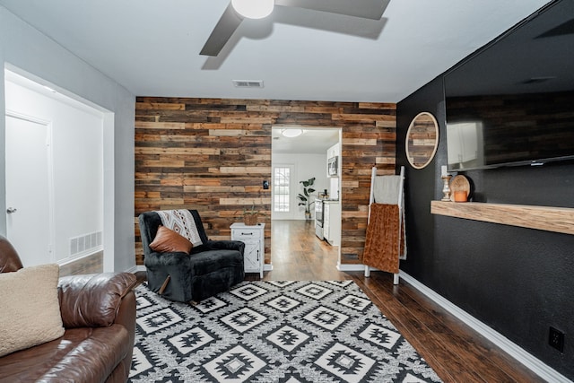 living room featuring wooden walls, dark wood-type flooring, and ceiling fan