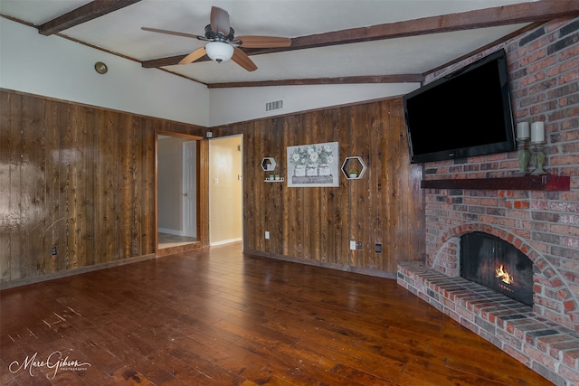 unfurnished living room featuring a fireplace, vaulted ceiling with beams, dark hardwood / wood-style flooring, brick wall, and wood walls