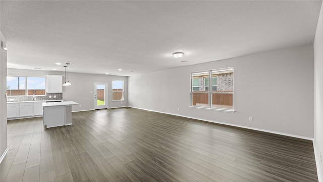 unfurnished living room with a textured ceiling, plenty of natural light, and dark hardwood / wood-style floors