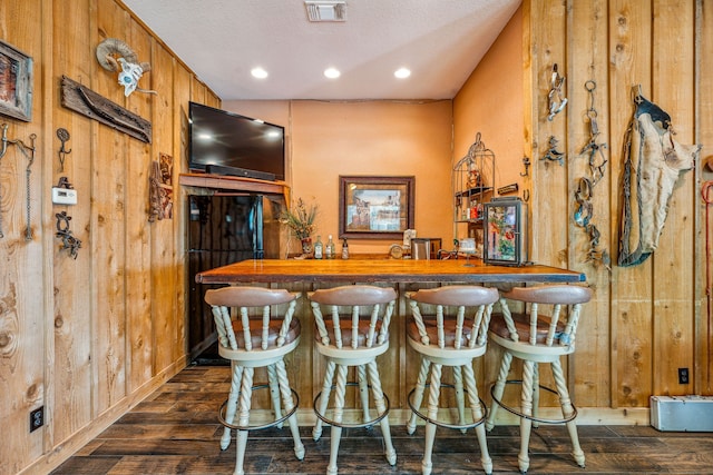 bar with dark hardwood / wood-style flooring, wood walls, and a textured ceiling