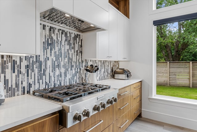 kitchen with backsplash, stainless steel gas stovetop, white cabinetry, and light stone countertops