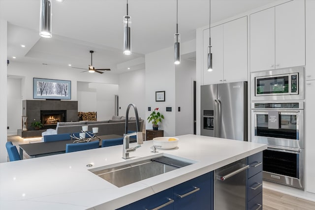 kitchen with pendant lighting, a tiled fireplace, stainless steel appliances, and ceiling fan