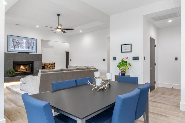 dining space featuring light hardwood / wood-style flooring, ceiling fan, a tray ceiling, and a tiled fireplace