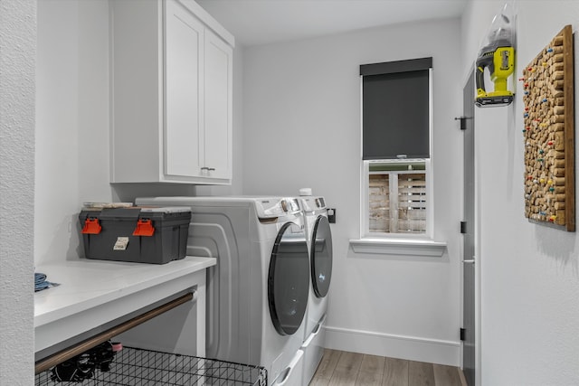 clothes washing area featuring wood-type flooring, washing machine and clothes dryer, and cabinets