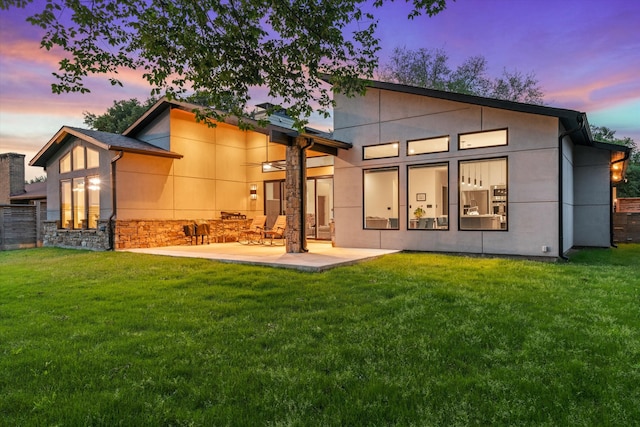 back house at dusk featuring a patio and a yard