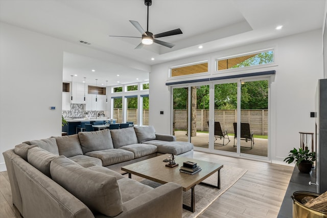 living room featuring a raised ceiling, ceiling fan, and light wood-type flooring