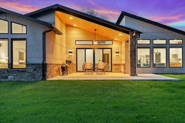 back house at dusk featuring a patio and a lawn