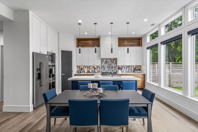 interior space featuring a center island with sink, backsplash, white cabinetry, and appliances with stainless steel finishes