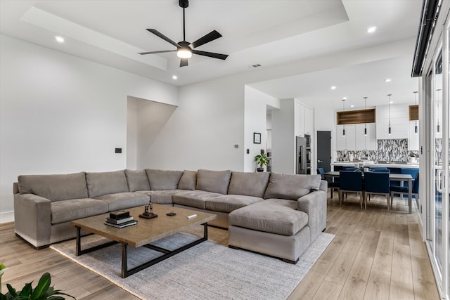 living room featuring a raised ceiling, ceiling fan, and light hardwood / wood-style floors