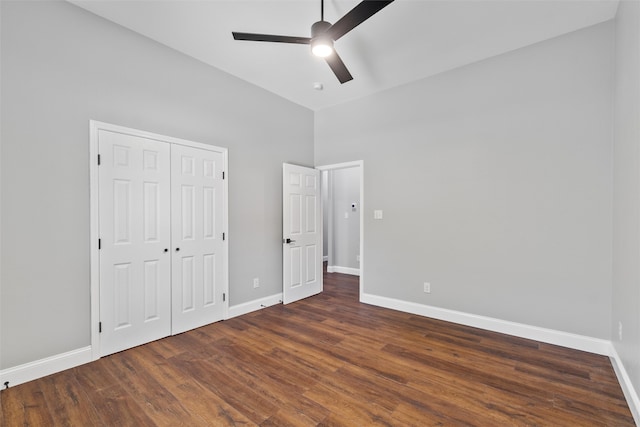 unfurnished bedroom featuring ceiling fan, a closet, a towering ceiling, and dark wood-type flooring