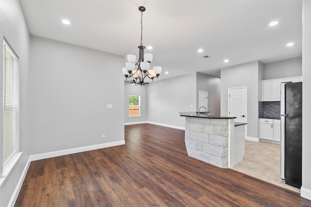 kitchen with white cabinetry, hardwood / wood-style flooring, black refrigerator, pendant lighting, and tasteful backsplash