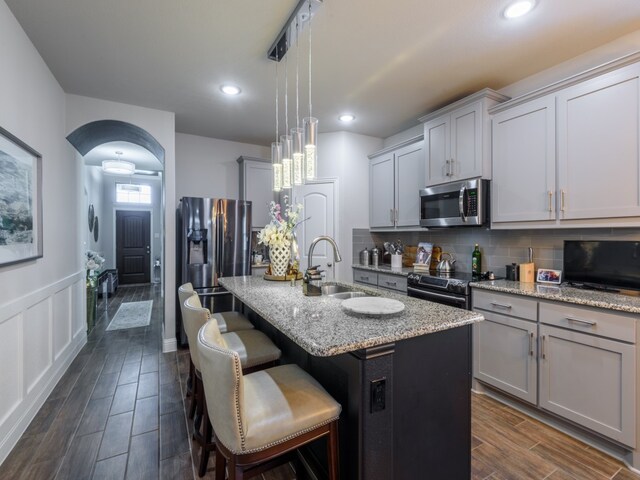 kitchen with decorative light fixtures, backsplash, appliances with stainless steel finishes, sink, and an island with sink