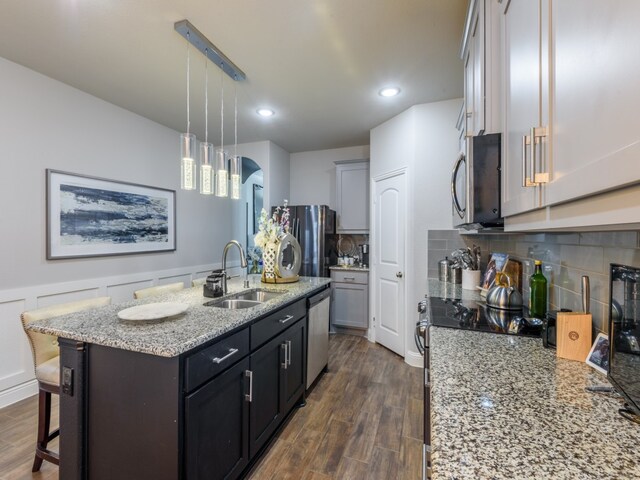 kitchen with appliances with stainless steel finishes, sink, backsplash, dark wood-type flooring, and a kitchen island with sink