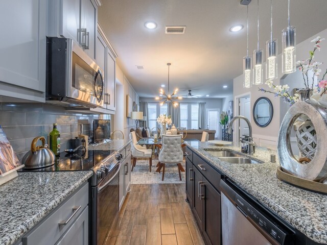 kitchen with appliances with stainless steel finishes, sink, tasteful backsplash, dark wood-type flooring, and pendant lighting