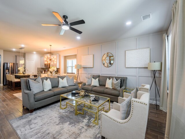 living room with ceiling fan with notable chandelier and dark wood-type flooring