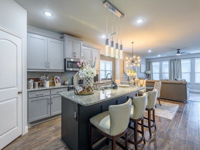 kitchen featuring ceiling fan with notable chandelier, a breakfast bar area, dark hardwood / wood-style floors, an island with sink, and pendant lighting