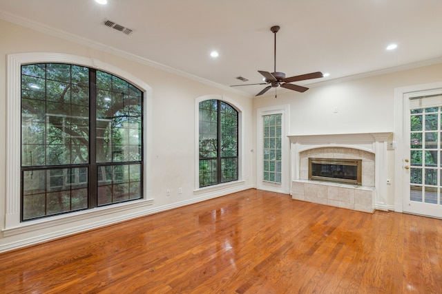 unfurnished living room with a healthy amount of sunlight, hardwood / wood-style flooring, a tiled fireplace, and ceiling fan