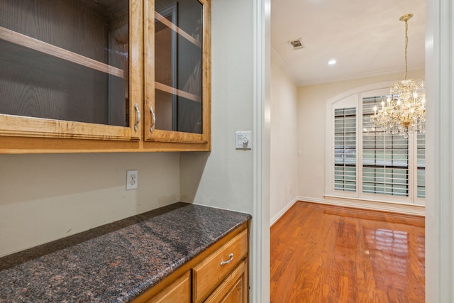 kitchen featuring crown molding, hanging light fixtures, dark stone countertops, hardwood / wood-style flooring, and a chandelier